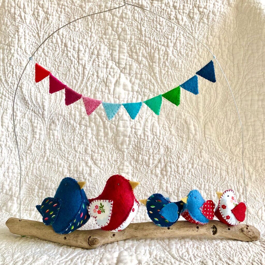 Handmade felt and fabric birds sitting on a natural driftwood and wire hanging perch with felt bunting detail.