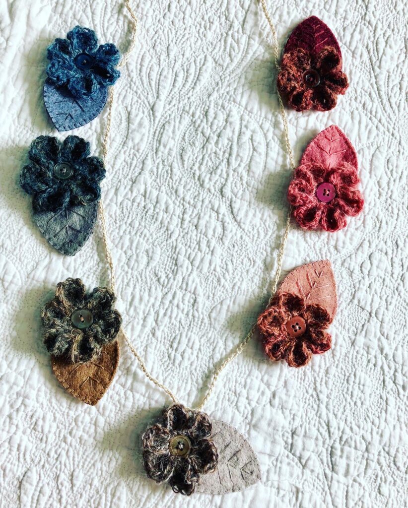 Handmade using 100% Alpaca wool and felt garland. A handmade, crocheted and sewn flower and leaf garland in a range of tonal hues. Burgundy through to Navy Blue. Seven Flower and leaf decorations along the garland.