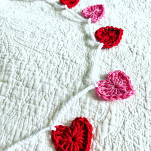 A garland of bright pink and red crocheted cotton hearts, on a white cotton chain.