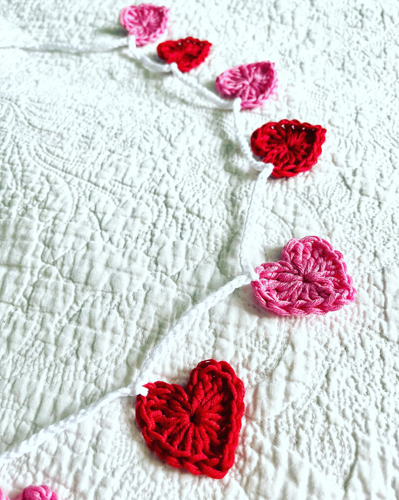 A garland of bright pink and red crocheted cotton hearts, on a white cotton chain.