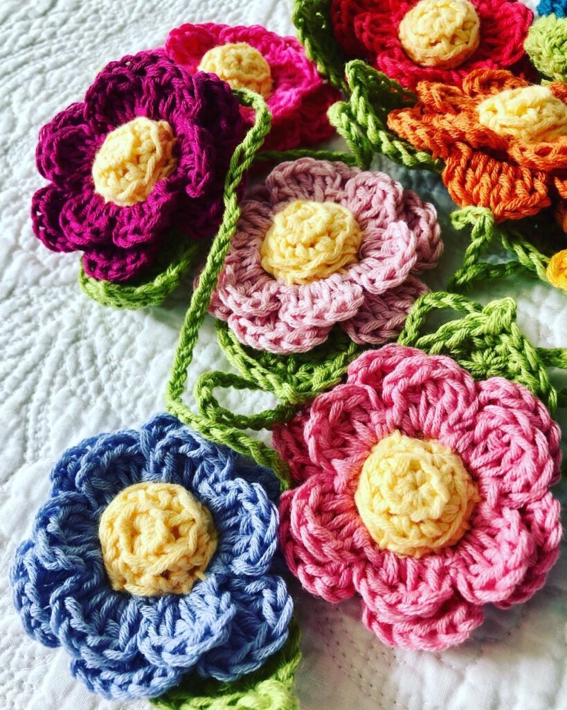 A hand crocheted garland of double layered flowers with crocheted centre and leaf details. Made in a rainbow of colours using 100% cotton.