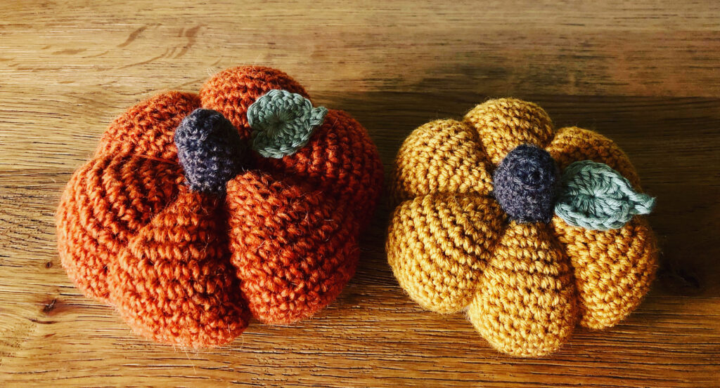 Crochet pumpkins in a selection of sizes and texture of 100% wool. In warm tones of orange or Mustard yellow with a brown stalk and green leaf detail.