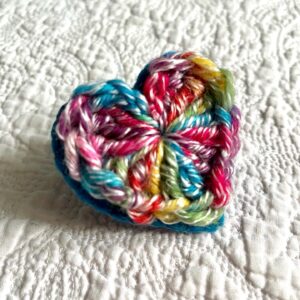 A bright, multicoloured crocheted heart on a turquoise hand stitched felt back with metal fixing brooch. Approximate size 5.5cm width x 5.5cm height.