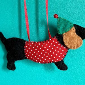 A hand made hanging decoration in the shape of a Dachshund dog. Hand cut and hand sewn in felt with a fabric coat and metal bell detail on the hat. The hanger is made of red ribbon. Approximate size 12.5cm w x 7cm h (excluding ribbon hanger) If more than one is required, please contact me directly to order. I am happy to take commissions.