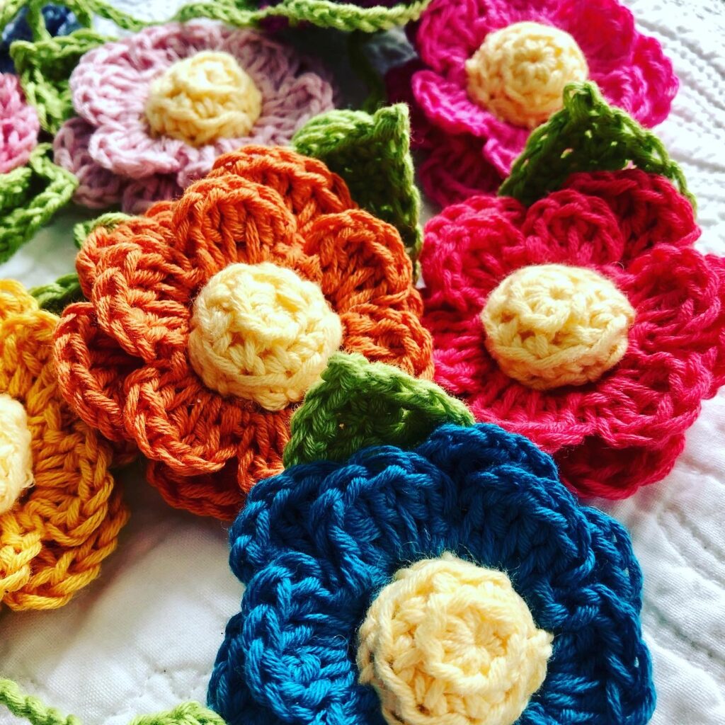 A hand crocheted garland of double layered flowers with crocheted centre and leaf details. Made in a rainbow of colours using 100% cotton.