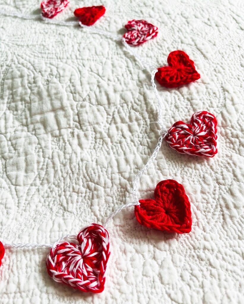 A garland of red and white and solid red crocheted cotton hearts, on a white cotton chain.