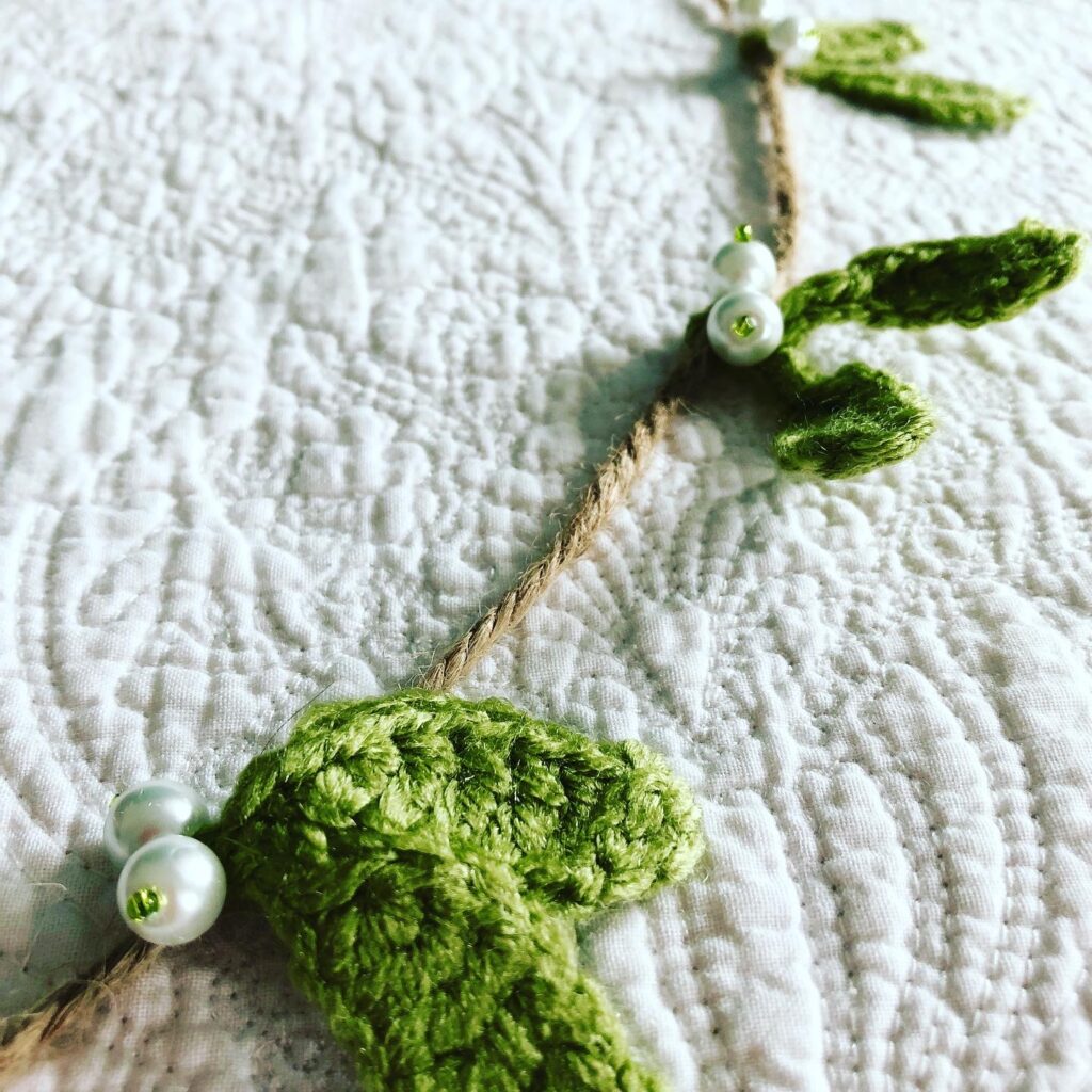 A hand crocheted mistletoe and beaded garland on jute.
