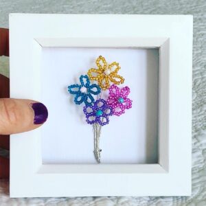 A small white wooden box frame displaying four small wire and glass bead flowers.