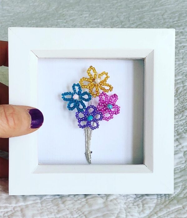 A small white wooden box frame displaying four small wire and glass bead flowers.