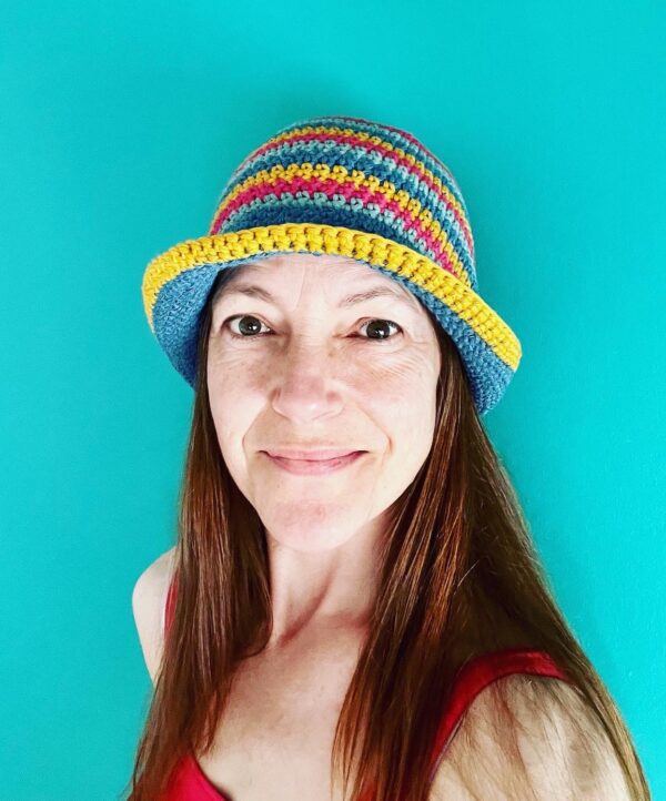 A hand crocheted bucket style hat, made using 100% cotton. It has multi coloured stripes in 3 bright colours, Turquoise, Mustard yellow and pink. One size.