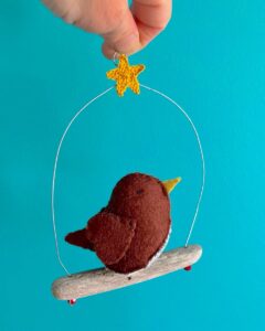 A single medium sized bird, handmade in brown felt with a cotton mistletoe print fabric chest. This bird is sat on a natural driftwood perch with a wire hanger that is decorated with a crocheted yellow star. Approximate size 11.5 cm width x 15cm height.