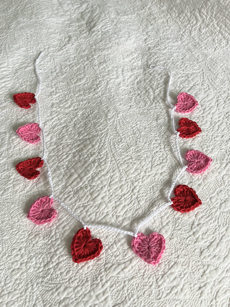 A garland of bright pink and red crocheted cotton hearts, on a white cotton chain.