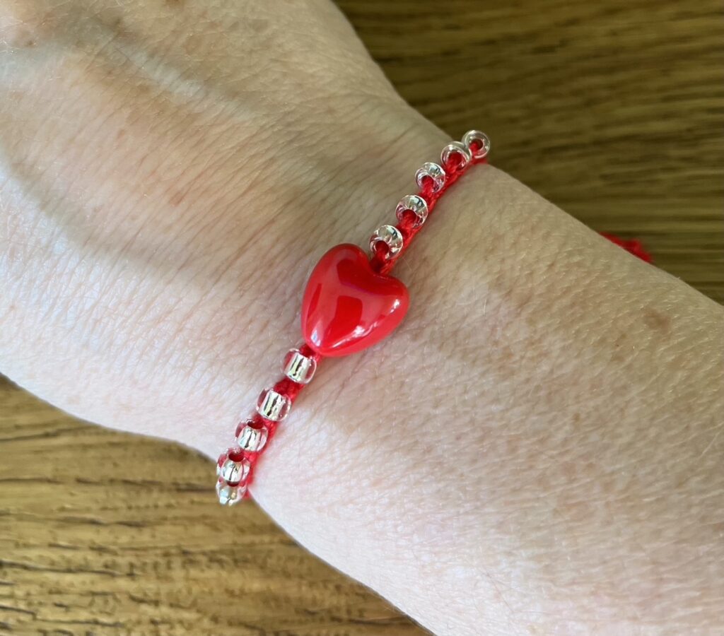 A red ceramic heart and clear glass beaded bracelet on a red crocheted cotton strap, with a fully adjustable sliding fastening.