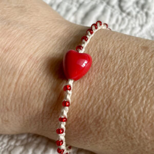 A red ceramic heart and red glass beaded bracelet on a cream crocheted cotton strap, with a fully adjustable sliding fastening.