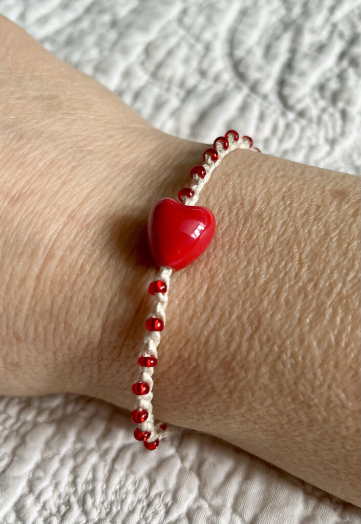 A red ceramic heart and red glass beaded bracelet on a cream crocheted cotton strap, with a fully adjustable sliding fastening.