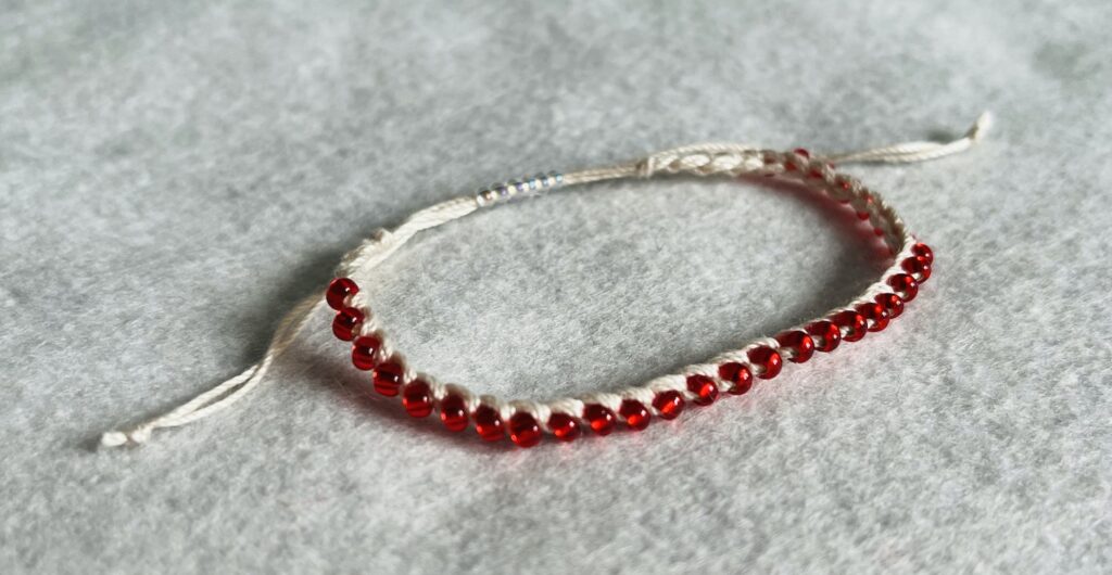 A red glass beaded bracelet on a cream crocheted cotton strap, with a fully adjustable sliding fastening.