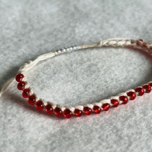 A red glass beaded bracelet on a cream crocheted cotton strap, with a fully adjustable sliding fastening.