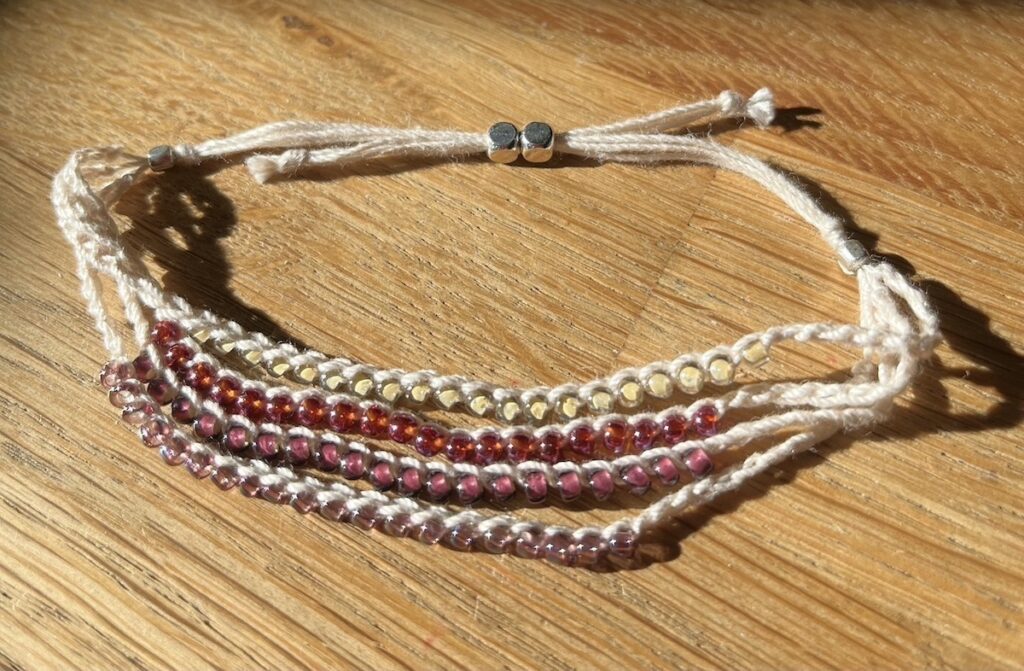 4 strand, fully adjustable bracelet with glass beads and silver metal coloured charm. Handmade using 100% cotton. Eco-friendly and fully recyclable.