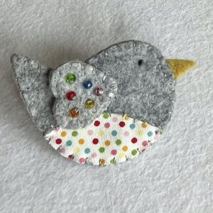 This little birdie brooch is completely hand cut, stitched embroidered and embellished. It is made using a wool mix felt and patterned fabric. It is hand embellished using glass beads and has a metal locking fixing on the back. Approximate size 6cm wide x 4cm height. 