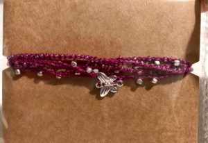 A purple cotton, multi stranded, crocheted bracelet with sliver coloured metal beads and a sliver coloured metal butterfly charm.