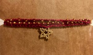 A burgundy coloured cotton, multi stranded, crocheted bracelet with gold coloured beads and a handmade star charm.