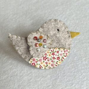 This little birdie brooch is completely hand cut, stitched embroidered and embellished. It is made using a wool mix felt and patterned fabric. It is hand embellished using glass beads and has a metal locking fixing on the back. Approximate size 6cm wide x 4cm height. 