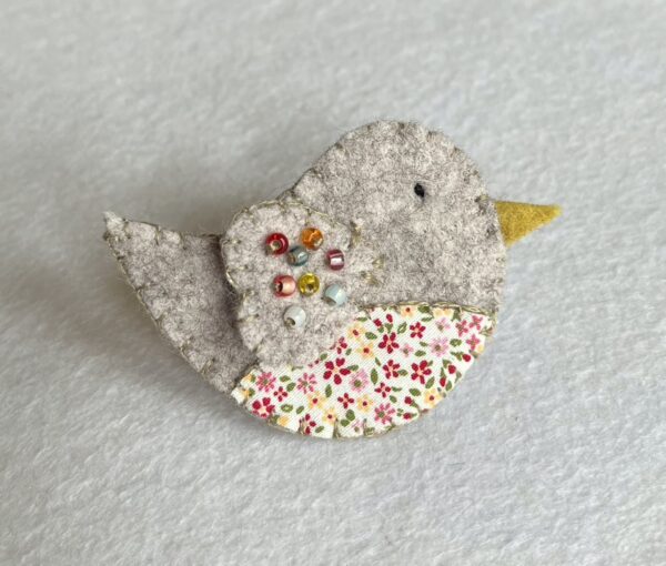 This little birdie brooch is completely hand cut, stitched embroidered and embellished. It is made using a wool mix felt and patterned fabric. It is hand embellished using glass beads and has a metal locking fixing on the back. Approximate size 6cm wide x 4cm height. 