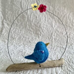 A single small sized bird, handmade in Turquoise coloured felt, with a cotton multi coloured dotty print fabric chest and hand embroidered/glass beaded detail on the wings. This bird is sat on a natural driftwood perch with a wire hanger that is decorated with a yellow and pink crocheted flowers.