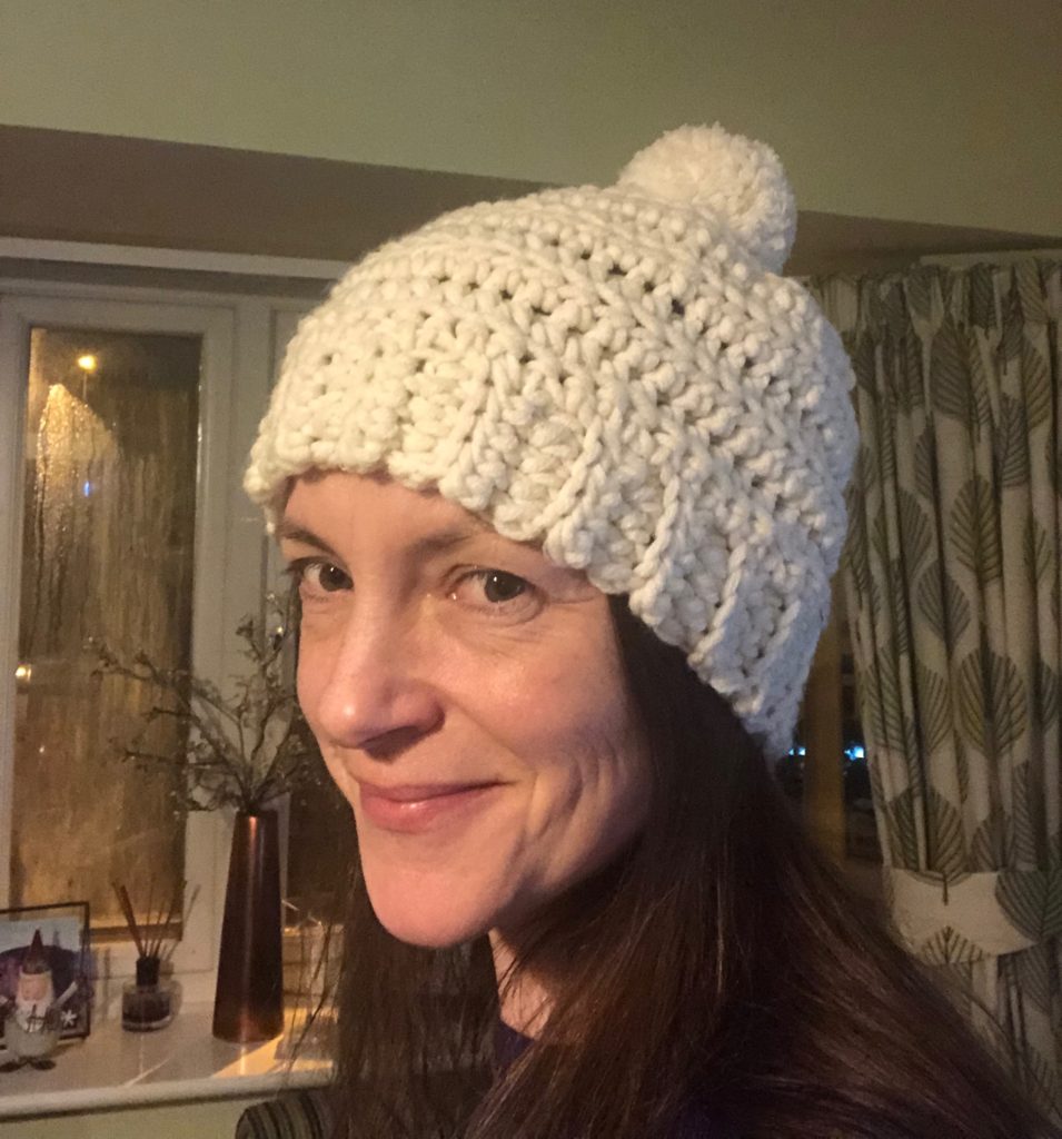A cream, chunky crocheted hat with pom-pom detail.