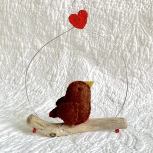 A single, small sized bird, handmade in brown felt with a red and white spotty cotton fabric chest. The bird is sat on a natural driftwood perch with a wire hanger that is decorated with a single red heart. Approximate size 11cm width x 14cm