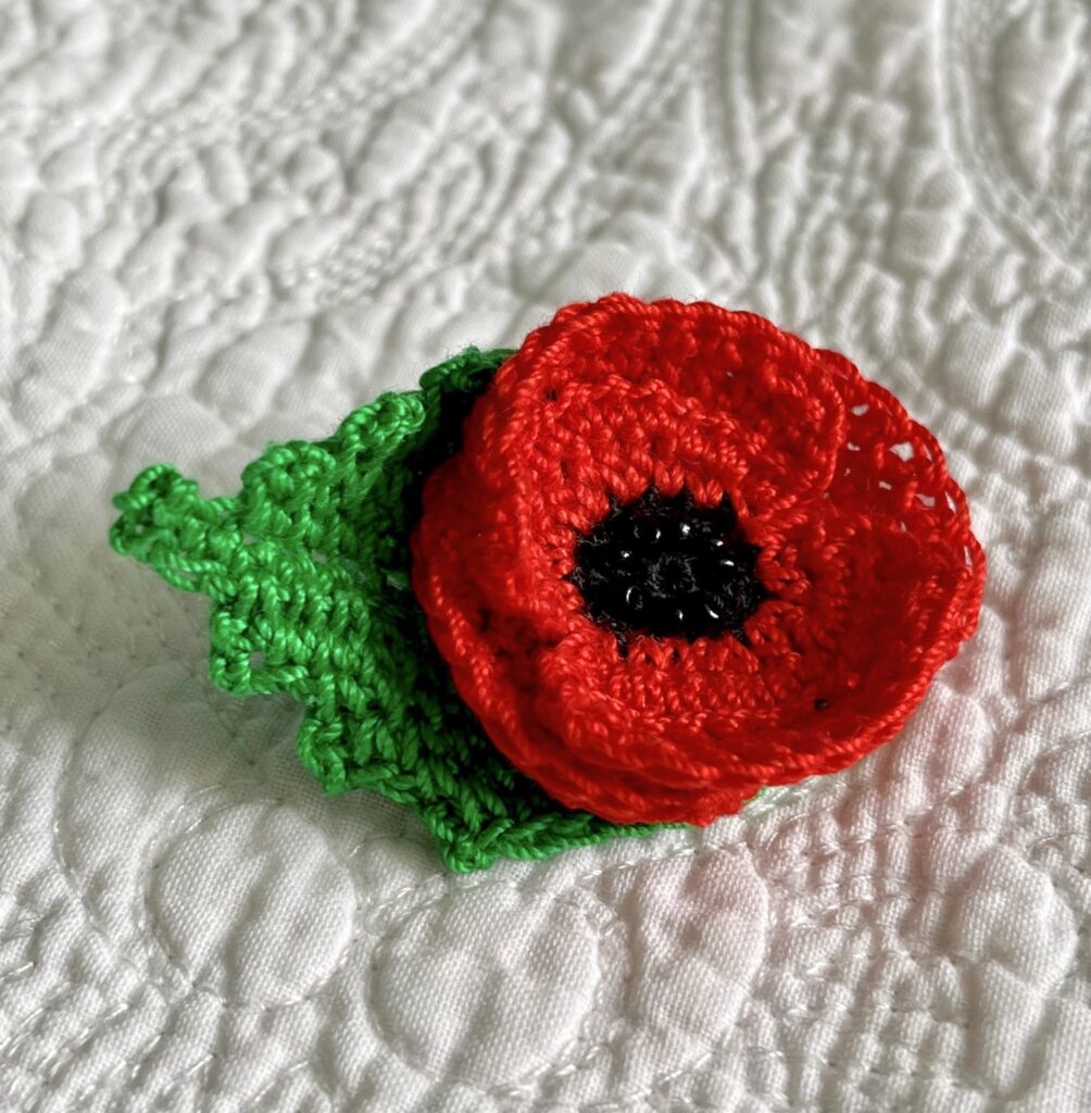 A small, double layered, red Poppy with black glass beaded detail and a green leaf. Handmade using 100% cotton, glass beads and a metal locking fastening on the back. Approximate size 6cm x 4cm.