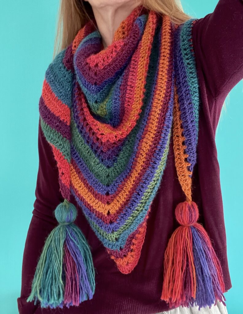 This large triangular wrap/shawl has been crocheted and is handmade. It has been crafted from a beautifully soft, supple and light-weight yarn in a rainbow of autumnal shades. The yarn is a mix of 90% Premium Acrylic and 10% Wool, which makes it extremely wearable and machine washable too. Approximate sizes 140cm wide (not including tassels) x 71cm height. Each tassel is approximately 16cm long. This item is machine washable on a hand wash setting at 30c. Gently re-shape and dry flat. Do not tumble dry.