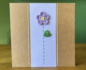 A single crocheted Lilac flower and green leaf, with a hand stitched detailing.

This medium brown card has a blank white insert for your own message, and an envelope is included.

Approximate size 12.5cm x 12.5 cm.

Made using 100% cotton.
Eco-friendly, Vegan friendly and fully recyclable.