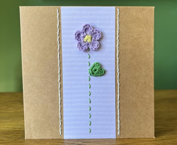 A single crocheted Lilac flower and green leaf, with a hand stitched detailing. This medium brown card has a blank white insert for your own message, and an envelope is included. Approximate size 12.5cm x 12.5 cm. Made using 100% cotton. Eco-friendly, Vegan friendly and fully recyclable.