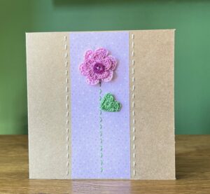 A single crocheted  flower with a double layer of Lilac petals and button, with a green leaf and hand stitched detailing.
This medium brown card has a blank white insert for your own message, and an envelope is included.
Approximate size 12.5cm x 12.5 cm.
Made using 100% cotton.
Eco-friendly, Vegan friendly and fully recyclable.