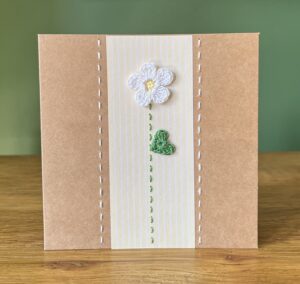 A single crocheted White flower and green leaf, with a hand stitched detailing.

This medium brown card has a blank white insert for your own message, and an envelope is included.

Approximate size 12.5cm x 12.5 cm.

Made using 100% cotton.
Eco-friendly, Vegan friendly and fully recyclable.
