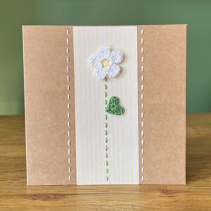 A single crocheted White flower and green leaf, with a hand stitched detailing. This medium brown card has a blank white insert for your own message, and an envelope is included. Approximate size 12.5cm x 12.5 cm. Made using 100% cotton. Eco-friendly, Vegan friendly and fully recyclable.