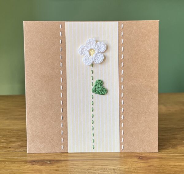 A single crocheted White flower and green leaf, with a hand stitched detailing. This medium brown card has a blank white insert for your own message, and an envelope is included. Approximate size 12.5cm x 12.5 cm. Made using 100% cotton. Eco-friendly, Vegan friendly and fully recyclable.