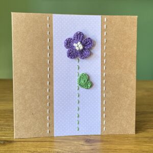 A single crocheted Purple flower and green leaf, with a hand stitched detailing. This medium brown card has a blank white insert for your own message, and an envelope is included. Approximate size 12.5cm x 12.5 cm. Made using 100% cotton. Eco-friendly, Vegan friendly and fully recyclable.