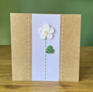 A single crocheted White flower and green leaf, with a hand stitched detailing. This medium brown card has a blank white insert for your own message, and an envelope is included. Approximate size 12.5cm x 12.5 cm. Made using 100% cotton. Eco-friendly, Vegan friendly and fully recyclable.