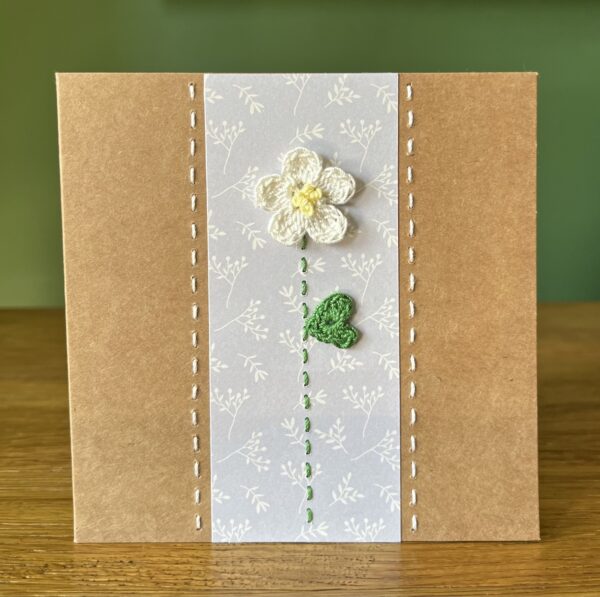 A single crocheted White flower and green leaf, with a hand stitched detailing. This medium brown card has a blank white insert for your own message, and an envelope is included. Approximate size 12.5cm x 12.5 cm. Made using 100% cotton. Eco-friendly, Vegan friendly and fully recyclable.