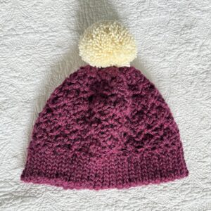 A soft and chunky textured hat with a large detachable bobble. Made in a warm cranberry colour using a very soft chunky but lightweight, 75% acrylic/ 25% Wool mix yarn. The bobble is made using a cream coloured 100% Wool. The perfect winter warmer!