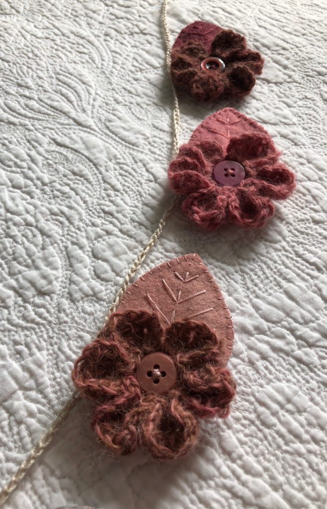 A handmade, crocheted and sewn flower and leaf garland in a range of tonal hues. Burgundy through to Navy Blue. Seven Flower and leaf decorations along the garland.