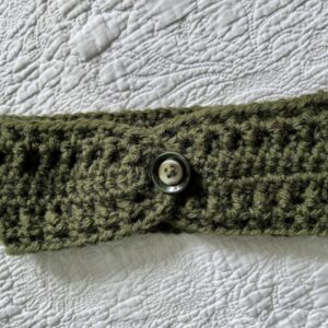 A hand crocheted, textured, ear warmer, in a warm green colour, with button detail. Made using a super soft, warm and chunky Acrylic 75% / Wool 25% mix yarn.