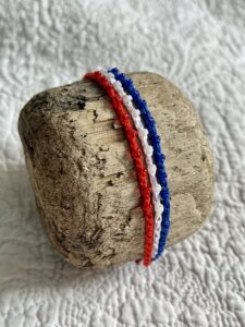 A handmade, crocheted and glass beaded bracelet. Fully adjustable. Made in 100% cotton in red, white and blue colours.