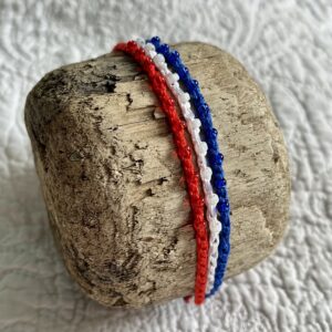 A handmade, crocheted and glass beaded bracelet. Fully adjustable. Made in 100% cotton in red, white and blue colours.