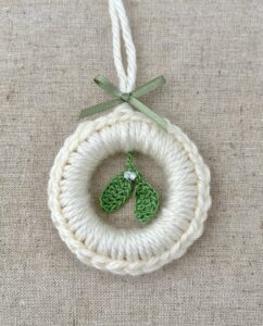 A crocheted and mini mistletoe embellished Christmas wreath, hanging decoration.

Handmade using a wooden ring with cream coloured yarn, 100% cotton in green and opal effect glass beaded embellishments.

Approximate size of wreath 8.5cm height x 7cm width. Not including hanging loop.