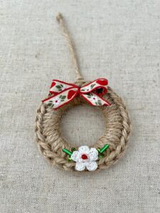 A crocheted and mini flower embellished Christmas wreath, hanging decoration. Handmade using a wooden ring with 100% natural coloured Jute, 100% cotton in white and glass beaded embellishments. Approximate size of wreath 8.5cm height x 7cm width. Not including hanging loop.