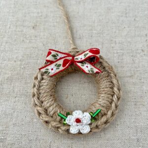 A crocheted and mini flower embellished Christmas wreath, hanging decoration. Handmade using a wooden ring with 100% natural coloured Jute, 100% cotton in white and glass beaded embellishments. Approximate size of wreath 8.5cm height x 7cm width. Not including hanging loop.