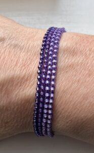 A handmade, crocheted and glass beaded bracelet. Fully adjustable with sliding metal bead fastening. 4 strands, made using 100% purple cotton and glass beads in 4 shades of purple.